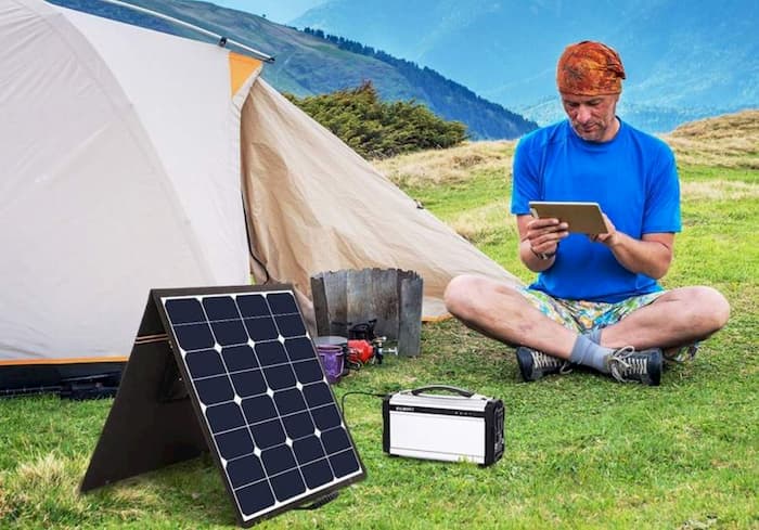 man camping on the mountain and sitting near portable foldable solar panels