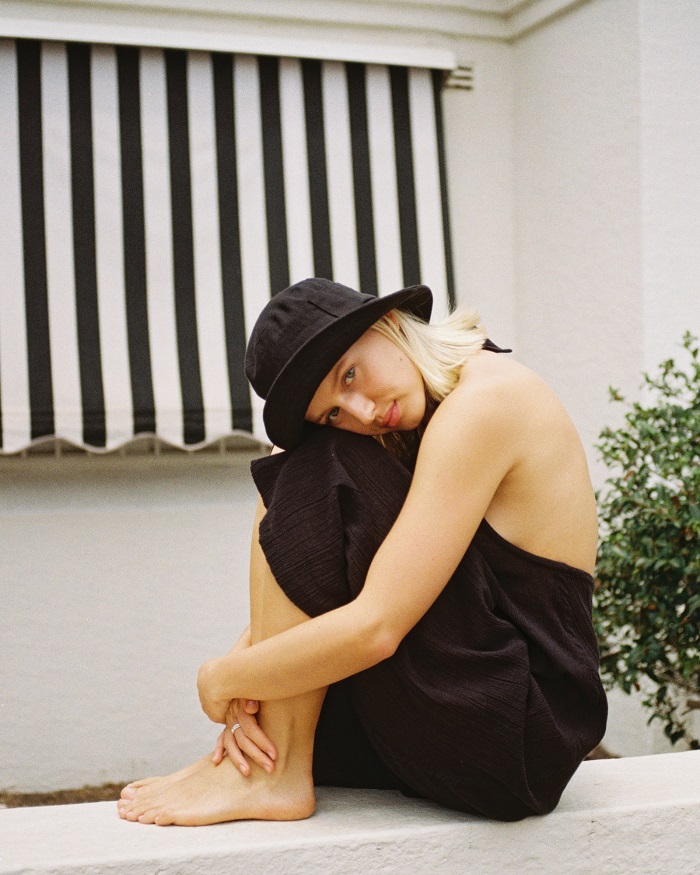 picture of a woman sitting on a concrete wearing black outfit and bucket hat