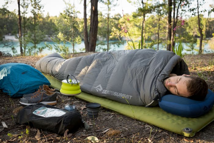 Man sleeping on a self inflating camping mat in the woods next to a river