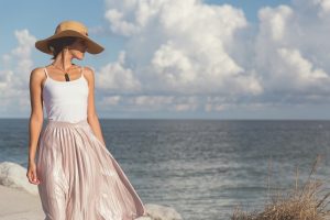 picture of a woman beside water and sky, wearing elegant summer outfit and a boater hat