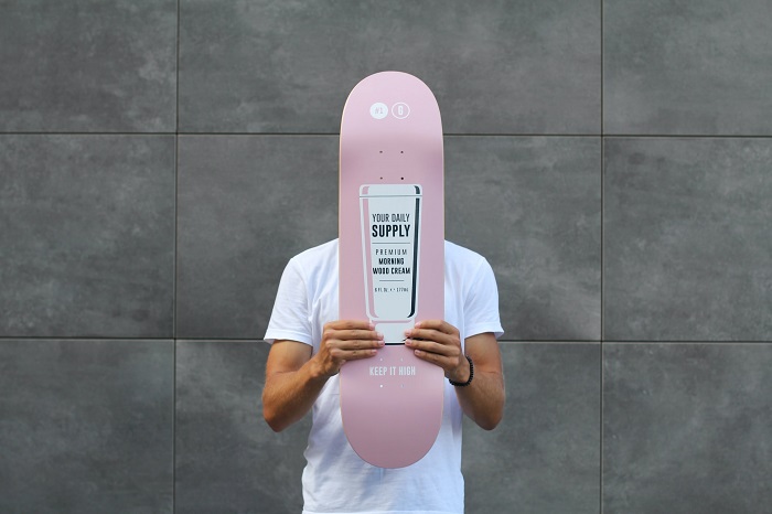 picture of a men in white shirt holding a pink skate deck standing in front a gray wall