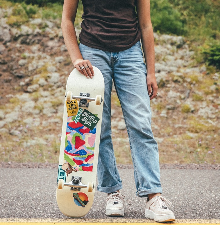 picture of a girl standing on a road beside a mountain holding a skate deck  