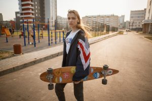 picture of a girl holding a skateboard standing on a road near buildings