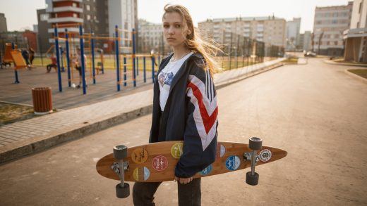 picture of a girl holding a skateboard standing on a road near buildings