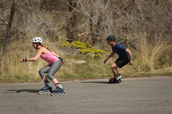 picture of a two persons riding inline roller skates on the road beside woods with protective gear