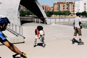 picture of persons riding roller skates in a park beside buildings wearing protective gear