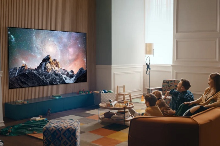 picture of a family sitting in a living room in front a large tv screen watching a movie