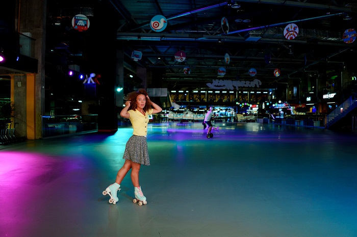 woman in yellow shirt and black and white skirt riding blue girls quad skates