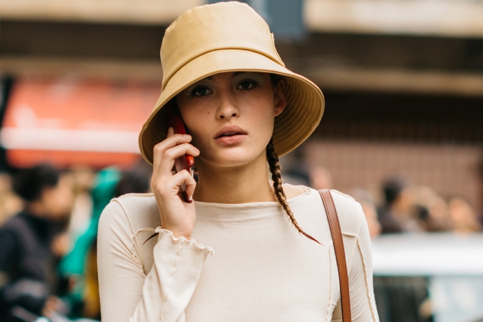 woman speaking on the phone, wearing bucket hat and white top