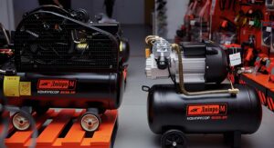 air compressor with a black tank on a bright orange stand in a tool shop.